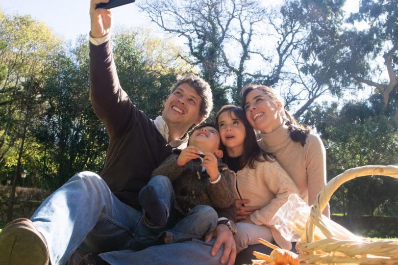 Happy family taking a selfie during a sunny picnic in a park.