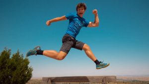 A young man jumping over a bench, expressing happiness and energy in the sunny outdoors of Spain.