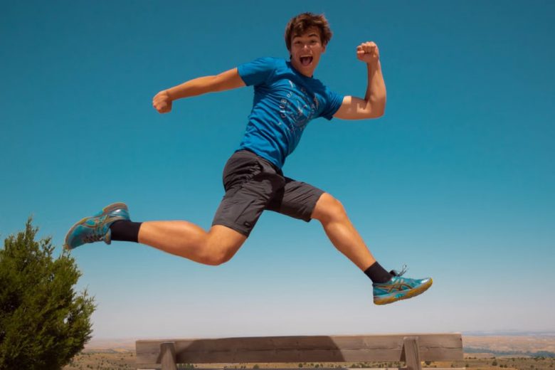 A young man jumping over a bench, expressing happiness and energy in the sunny outdoors of Spain.